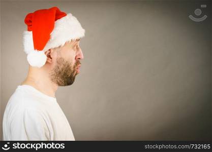 Bearded man wearing santa claus hat surprised expression, side view on grey with copy space. Christmes time.. Surpriced man in santa claus hat