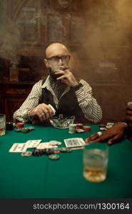 Bearded poker player with cigar, casino. Games of chance addiction. Man leisures in gambling house. Cards, chips and whiskey on gaming table with green cloth