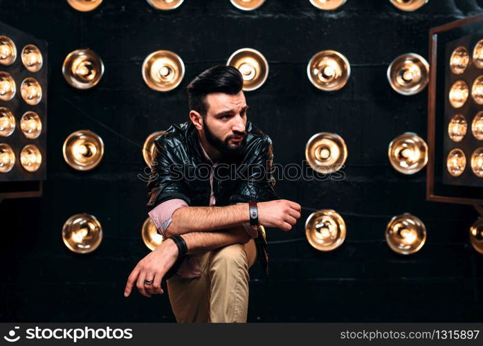 Bearded singer in black leather jacket on the stage with the decorations of lights