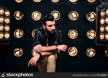 Bearded singer in black leather jacket on the stage with the decorations of lights