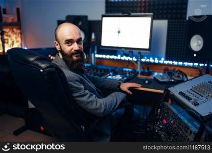 Bearded sound engineer at remote control panel in audio recording studio. Musician at the mixer, professional music mixing