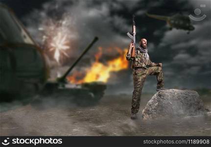 Bearded terrorist holding the kalashnikov rifle up. Terrorism and terror, soldier in khaki camouflage, military helicopter and tank on background. Bearded terrorist holding the kalashnikov rifle up