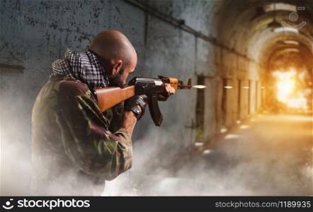Bearded terrorist shoots from a rifle, explosion and fire at the end of the corridor on background. Terrorism and terror, soldier in khaki camouflage fires to his enemy. Terrorist shoots from rifle, explosion in corridor