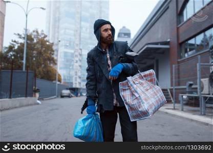 Bearded tramp man with bag on city street. Poverty is a social problem, homelessness and loneliness, alcoholism and drunk addiction, urban lonely. Bearded tramp man with bag on city street