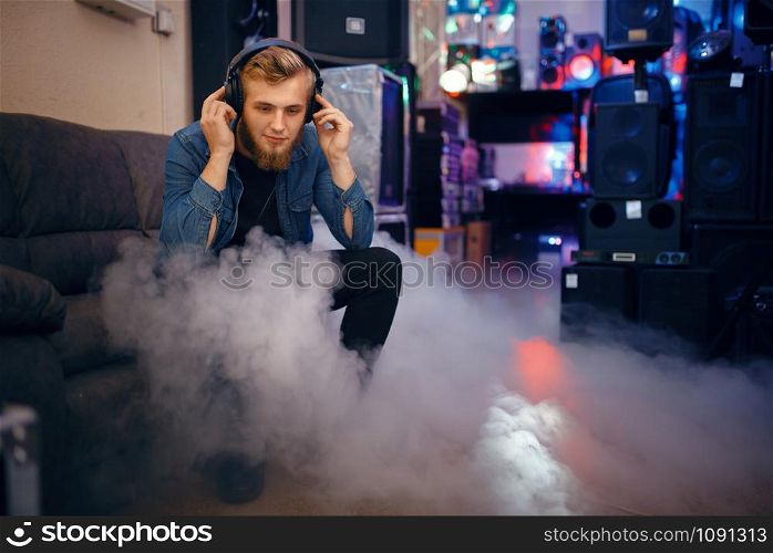 Bearded young musician choosing headphones in music store. Assortment in musical instrument shop, professional equipment for performers