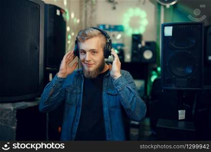 Bearded young musician choosing headphones in music store. Assortment in musical instrument shop, professional equipment. Young musician choosing headphones in music store