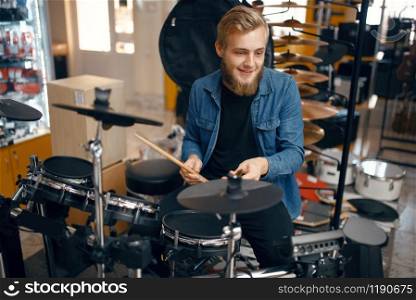 Bearded young musician plays on drum set in music store. Assortment in musical instrument shop, professional equipment for performers. Young musician plays on drum set in music store