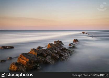 Beautfiul long exposure landscape of sea over rocks at sunset