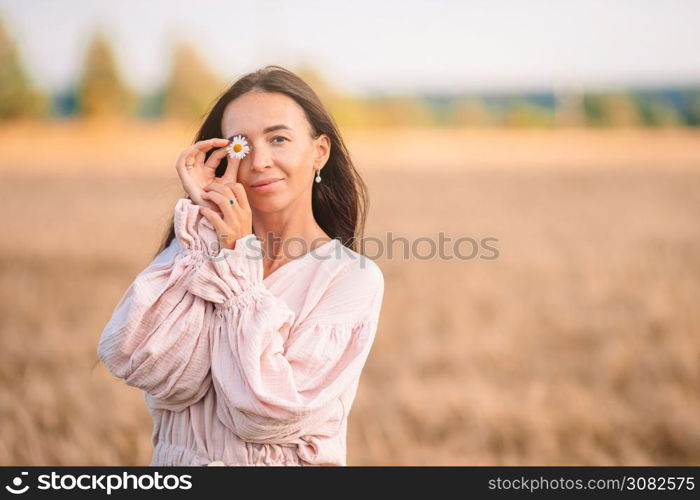 Beautful woman covered her eyes with chamomile in wheat field. Beautiful woman in dress in wheat field