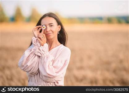 Beautful woman covered her eyes with chamomile in wheat field. Beautiful woman in dress in wheat field