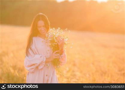 Beautful woman in wheat field with a bouquet of chamomile at sunset. Back view of girl in wheat field. Beautiful woman with ripe wheat in hands