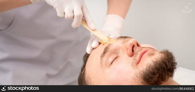 Beautician applying wax paste between eyebrows during the procedure of waxing in the beauty salon. Beautician applying wax paste between eyebrows during the procedure of waxing in the beauty salon.