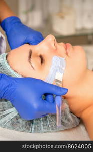 Beautician covering woman facial skin with moisturizing cleansing mask during skin care procedure in a spa beauty salon. Beautician covering woman facial skin with moisturizing cleansing mask during skin care procedure in a spa beauty salon.