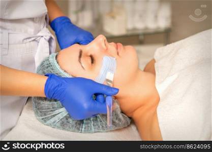 Beautician covering woman facial skin with moisturizing cleansing mask during skin care procedure in a spa beauty salon. Beautician covering woman facial skin with moisturizing cleansing mask during skin care procedure in a spa beauty salon.