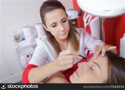 beautician hands doing eyebrow tattoo on woman face