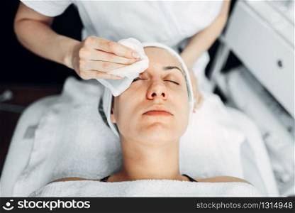 Beautician hands rubs the cream on female patient face, top view, cosmetology clinic. Facial skincare, rejuvenation procedure in spa salon. Beautician hands on female patient face, top view