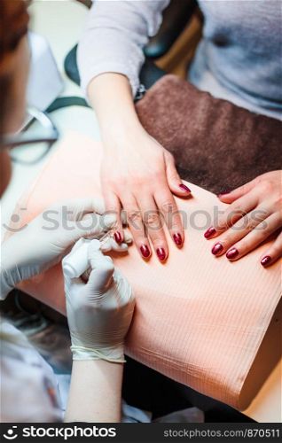 Beautician in a beauty salon doing a hybrid manicure. Painting and styling nails. Woman getting professional nails treatment. Close up of hands