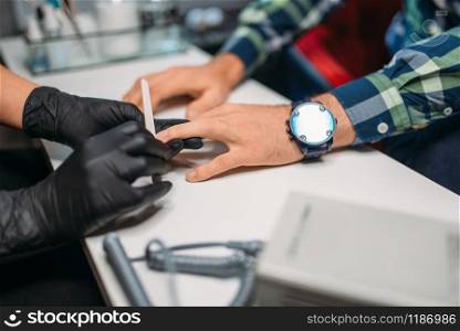Beautician in black gloves polishing nails to male client, top view, men manicure in salon. Manicurist doing hands care procedure