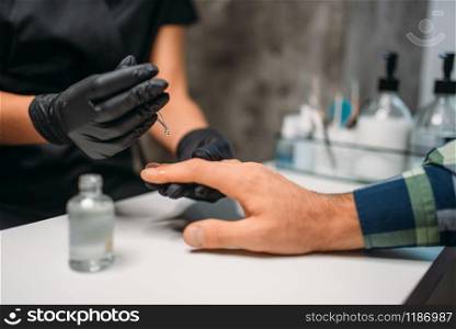 Beautician in black gloves polishing nails to male client, top view, men manicure in salon. Manicurist doing hands care procedure. Beautician polishing nails to male client in salon