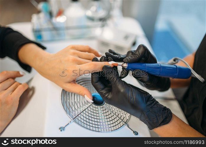 Beautician in black gloves sticks the nails of the client, manicure in salon. Manicurist doing hands care cosmetic procedure. Beautician in gloves sticks nails of the client