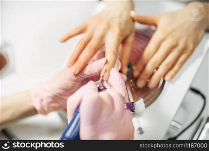 Beautician in gloves polishing nails of female client, top view, manicure in beauty salon. Manicurist doing hands care cosmetic procedure