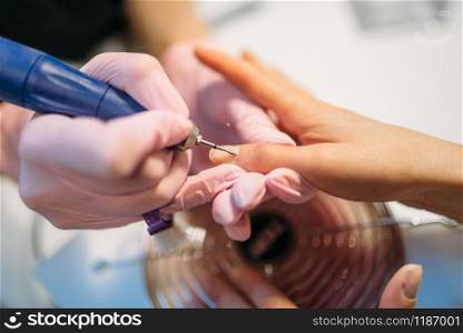 Beautician in gloves polishing nails of female client, top view, manicure in beauty salon. Manicurist doing hands care cosmetic procedure. Beautician polishing nails of client, top view
