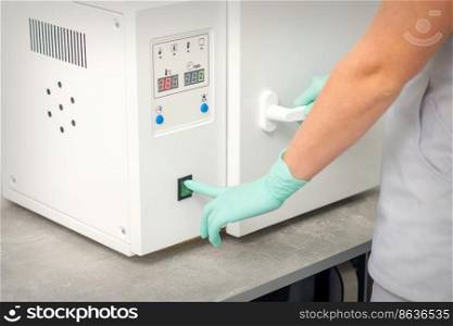 Beautician in protective gloves starts the machine for disinfection of tools before the depilation procedure. Beautician in protective gloves starts the machine for disinfection of tools before the depilation procedure.