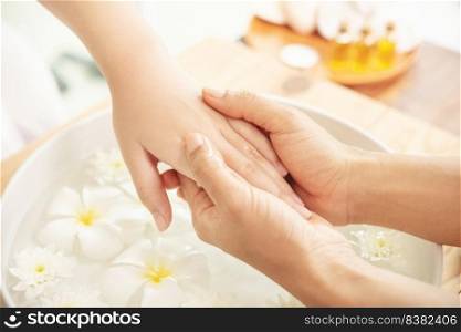 Beautician massaging hand of female spa salon client. Spa treatment and product for female feet and hand spa. white flowers in ceramic bowl with water for aromatherapy at spa.
