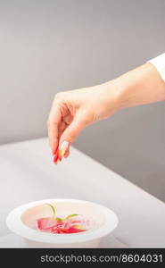 Beautician&rsquo;s female hands preparing manicure bath with red and pink roses petals on the table in spa. Beautician preparing manicure bath with petals