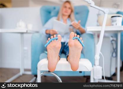 Beautician salon, foot care procedure. Legs treatment for female client in beauty shop, customer sitting in armchair, relaxation before pedicure