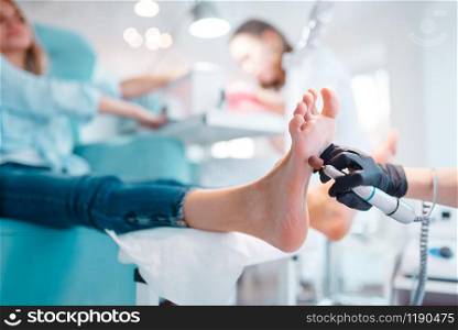 Beautician salon, foot polish procedure. Legs care treatment for female client in beauty shop, master in gloves works with customer, relaxation