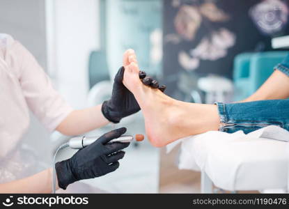 Beautician salon, foot polish procedure. Legs care treatment for female client in beauty shop, master in gloves works with customer, relaxation. Beautician salon, foot polish procedure