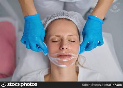 Beautician washes woman face using cotton pads to remove face mask. Facial cleansing procedure, cosmology service and beauty treatment concept. Beautician washes woman face using cotton pads to remove face mask