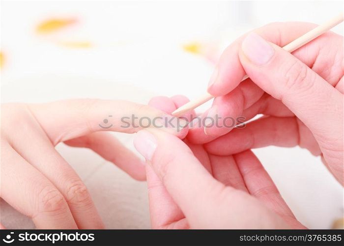 Beautician with cosmetic stick cleaning cuticles hands of female client. Manicure and skincare. Woman in beauty spa salon.