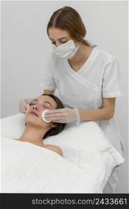 beautician with female client salon face care routine with cleansing disks