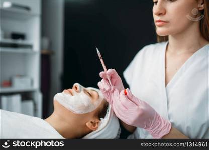 Beautician with syringe in hands against female patient, botox injection, getting rid of wrinkles, cosmetology clinic. Facial skincare, rejuvenation procedure in spa salon. Beautician with syringe in hands, botox injection