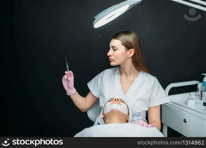 Beautician with syringe in hands against female patient, botox injection, getting rid of wrinkles, cosmetology clinic. Facial skincare, rejuvenation procedure in spa salon, health care. Beautician with syringe in hands, botox injection