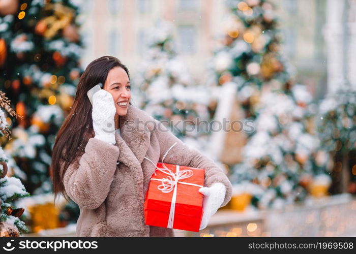 Beautidul girl with red gift on Christmas with smartphone in the snow outdoors. Happy girl near fir-tree branch in snow for new year.