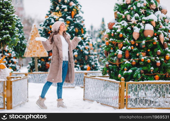 Beautidul woman near Christmas tree in the snow outdoors. Happy girl near fir-tree branch in snow for new year.