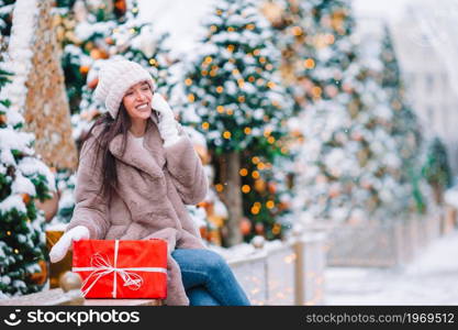 Beautidul woman with red gift on Christmas with smartphone. Happy girl near fir-tree branch in snow for new year.