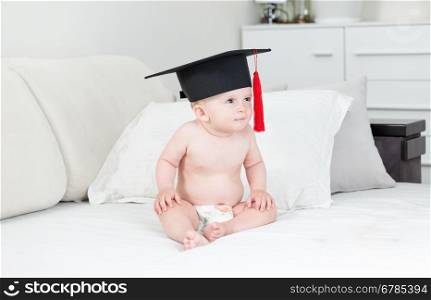 Beautiful 10 months old baby boy sitting on sofa and wearing graduation cap