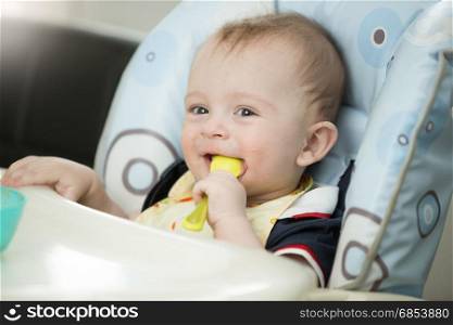Beautiful 9 month baby boy playing with spoon while eating