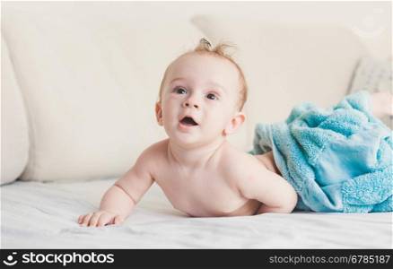 Beautiful 9 months baby boy under blue towel on bed with white sheets