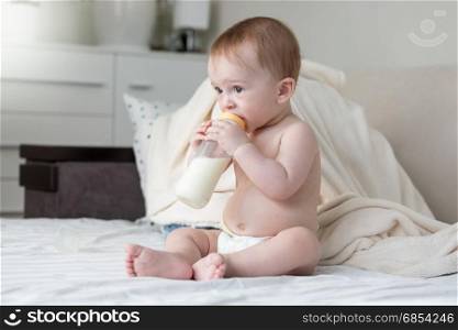 Beautiful 9 months old baby boy sitting on bed and drinking milk