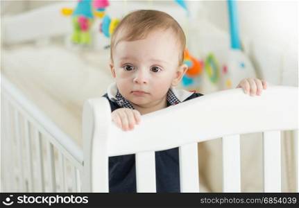 Beautiful 9 months old baby boy standing in white crib