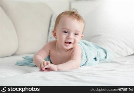 Beautiful 9 months old baby boy under blue towel lying on sofa at living room
