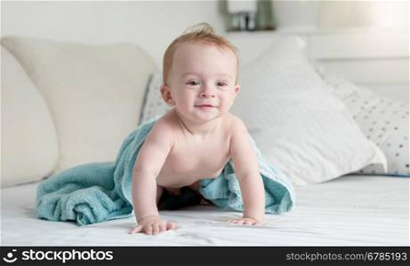 Beautiful 9 months old baby in blue towel after shower crawling on bed