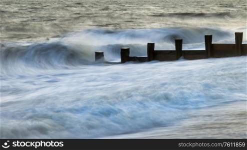 Beautiful abstract long exposure landscape image of waves crashing onto groynes on beach during sunset