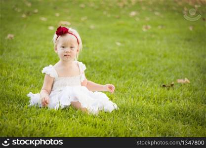 Beautiful Adorable Little Girl Wearing White Dress Sitting In A Grass Field.