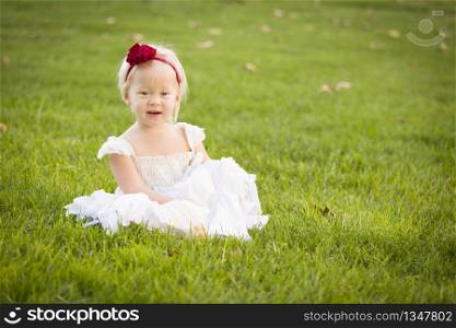 Beautiful Adorable Little Girl Wearing White Dress Sitting In A Grass Field.